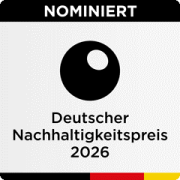 Logo der Nominierung für den Deutschen Nachhaltigkeitspreis 2026. Oben steht in weißer Schrift auf schwarzem Hintergrund das Wort 'NOMINIERT'. Darunter befindet sich ein schwarzes rundes Symbol mit einem kleinen weißen Kreis oben rechts darin. Unter dem Symbol steht: 'Deutscher Nachhaltigkeitspreis 2026'. Unten am Rand verläuft ein Streifen in den Farben Schwarz-Rot-Gold.